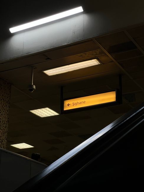 View of an underground station platform seen through an oval window, showing a wall with wooden paneling in rectangular blocks of varying warm brown tones. The platform surface appears clean with a me